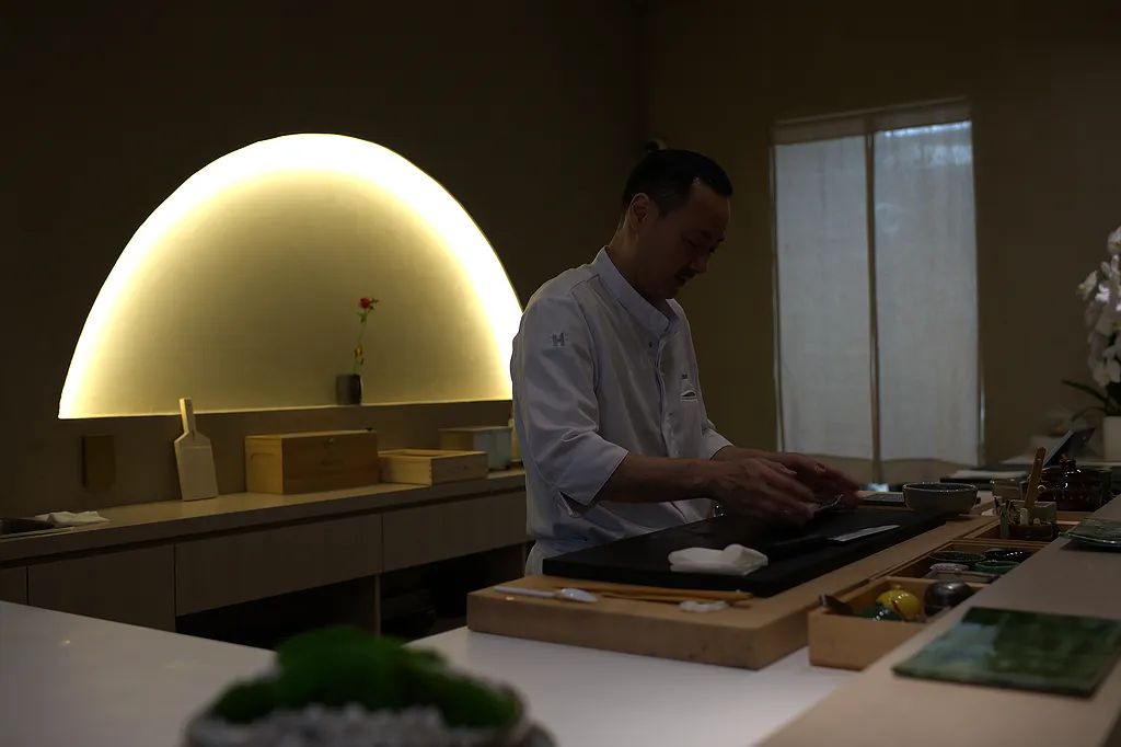 Chef Atsutaka Chikaraishi at the counter beneath the arched light