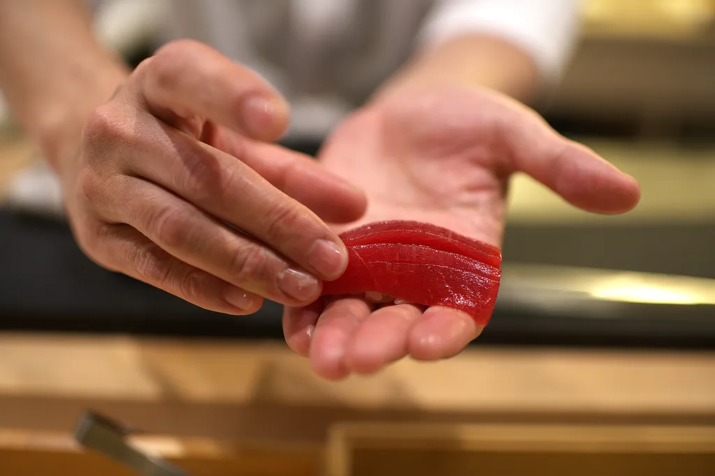 A single slice of bluefin tuna held in the chef's fingers above the counter