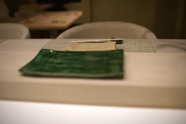 Chopsticks at rest on a folded napkin beside a green ceramic plate