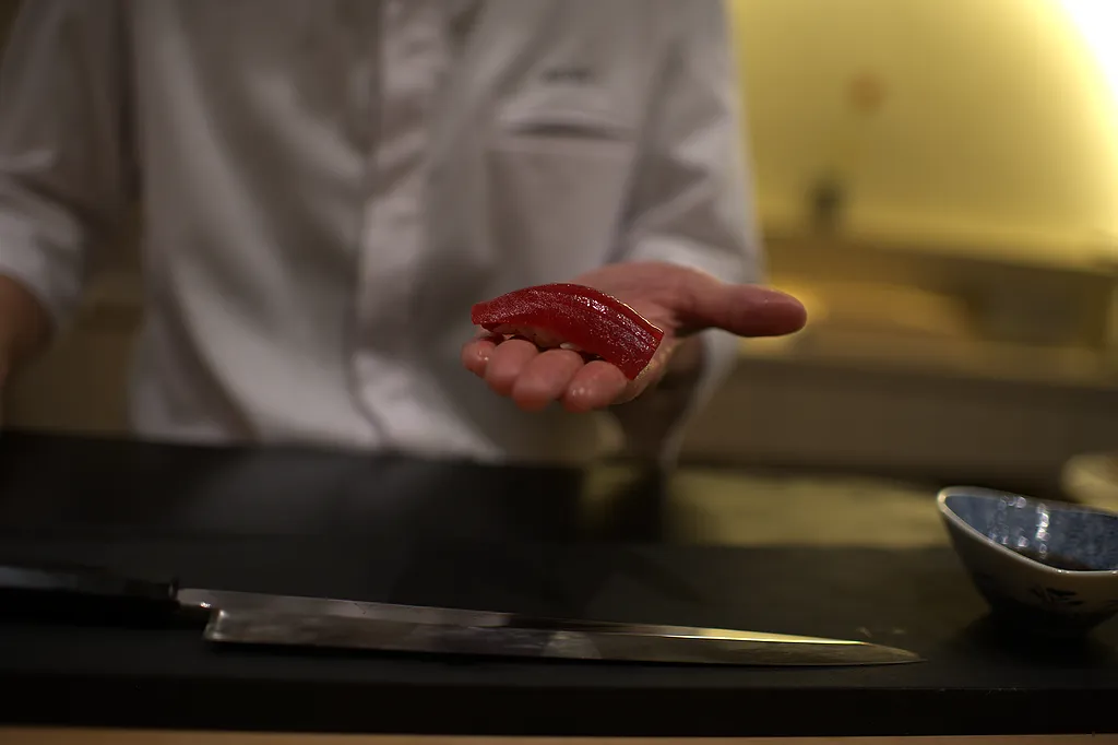 A piece of tuna nigiri resting on the chef's open palm, the seasoned rice visible beneath the fish