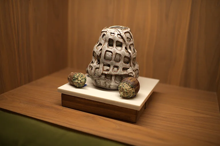 A pierced ceramic vessel on a walnut plinth